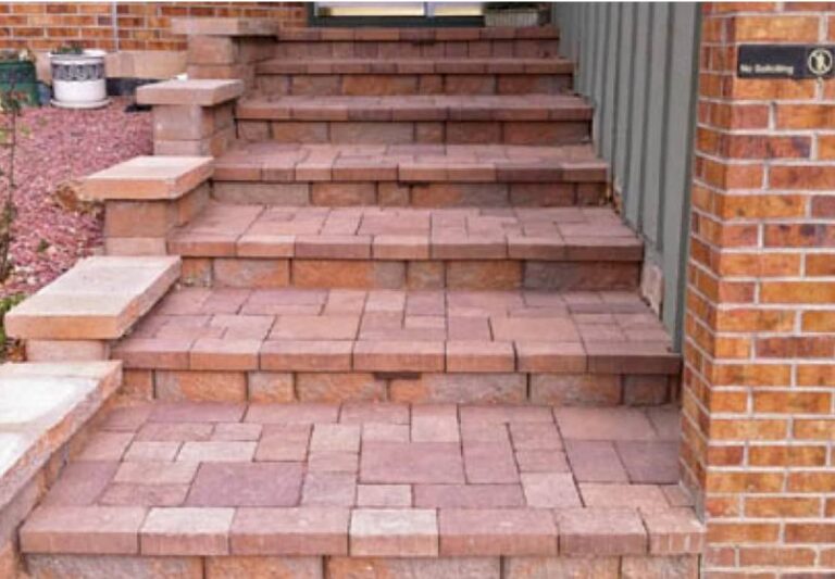 Brick steps with a pattern of rectangular and square bricks leading up to a doorway, bordered by brick walls on both sides.